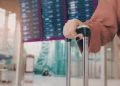 Traveler at an international airport holding passport and travel insurance documents before boarding a flight abroad.